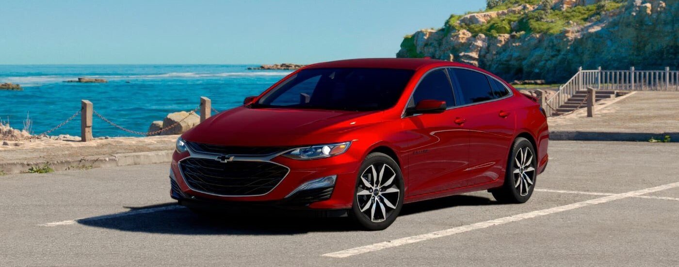 A red 2024 Chevy Malibu is show parked on a lot near the ocean.