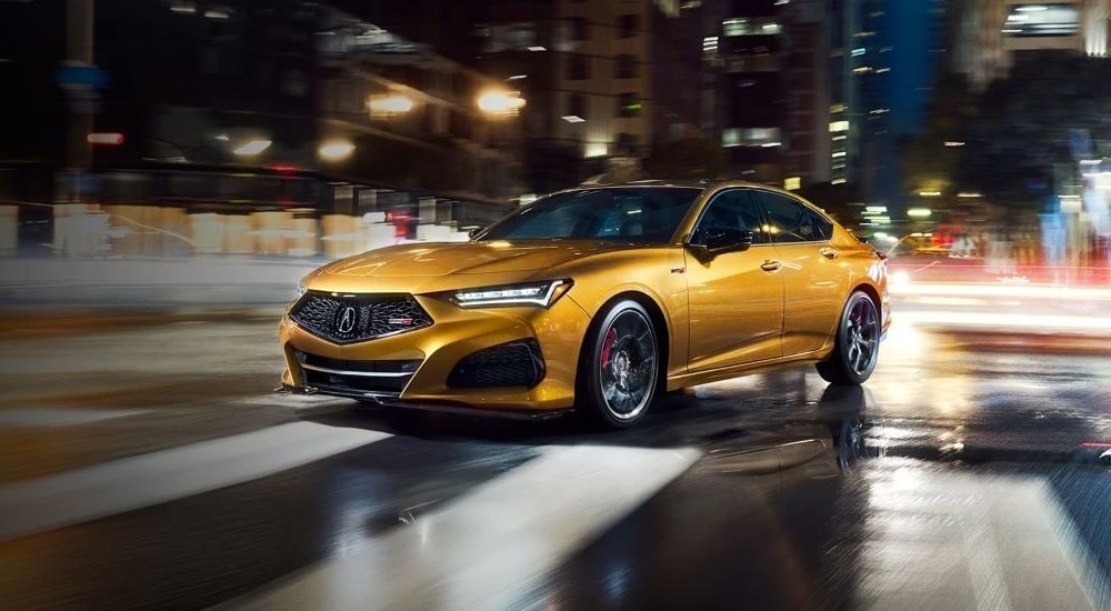 A yellow 2022 Acura TLX Type S is shown driving through a wet city intersection at night.