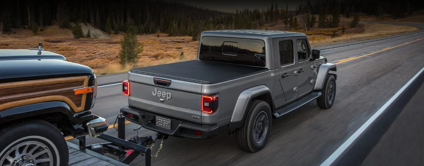 Grey 2022 Jeep Gladiator towing a vehicle down a road.