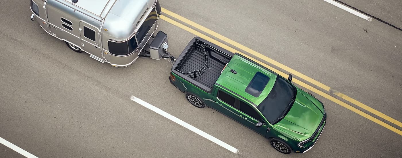 Green 2025 Ford Maverick towing a silver camper trailer on a highway